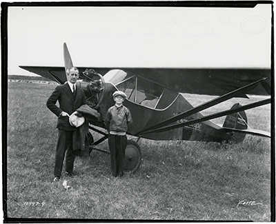 a man and a boy next to an 1920s Monocoupe aircraft